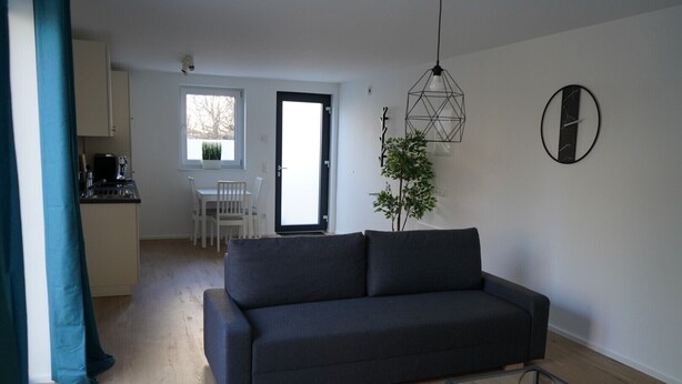 Ett modernt vardagsrum med en mörk soffa, ett soffbord i glas och en matplats med ett vitt bord och stolar.