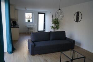 Een moderne woonkamer met een donkere bank, een glazen salontafel en een eethoek met een witte tafel en stoelen.
