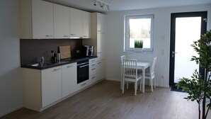 Ett modernt kök med vita skåp, en svart bänkskiva och ett fönster ovanför matbordet.