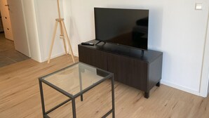 Ett modernt vardagsrum med en platt-TV placerad på ett mörkt träskåp, ett soffbord i glas och en golvlampa.