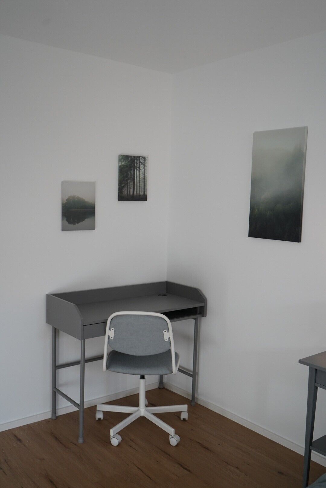 A room with a desk, a chair, and three framed pictures on the wall.