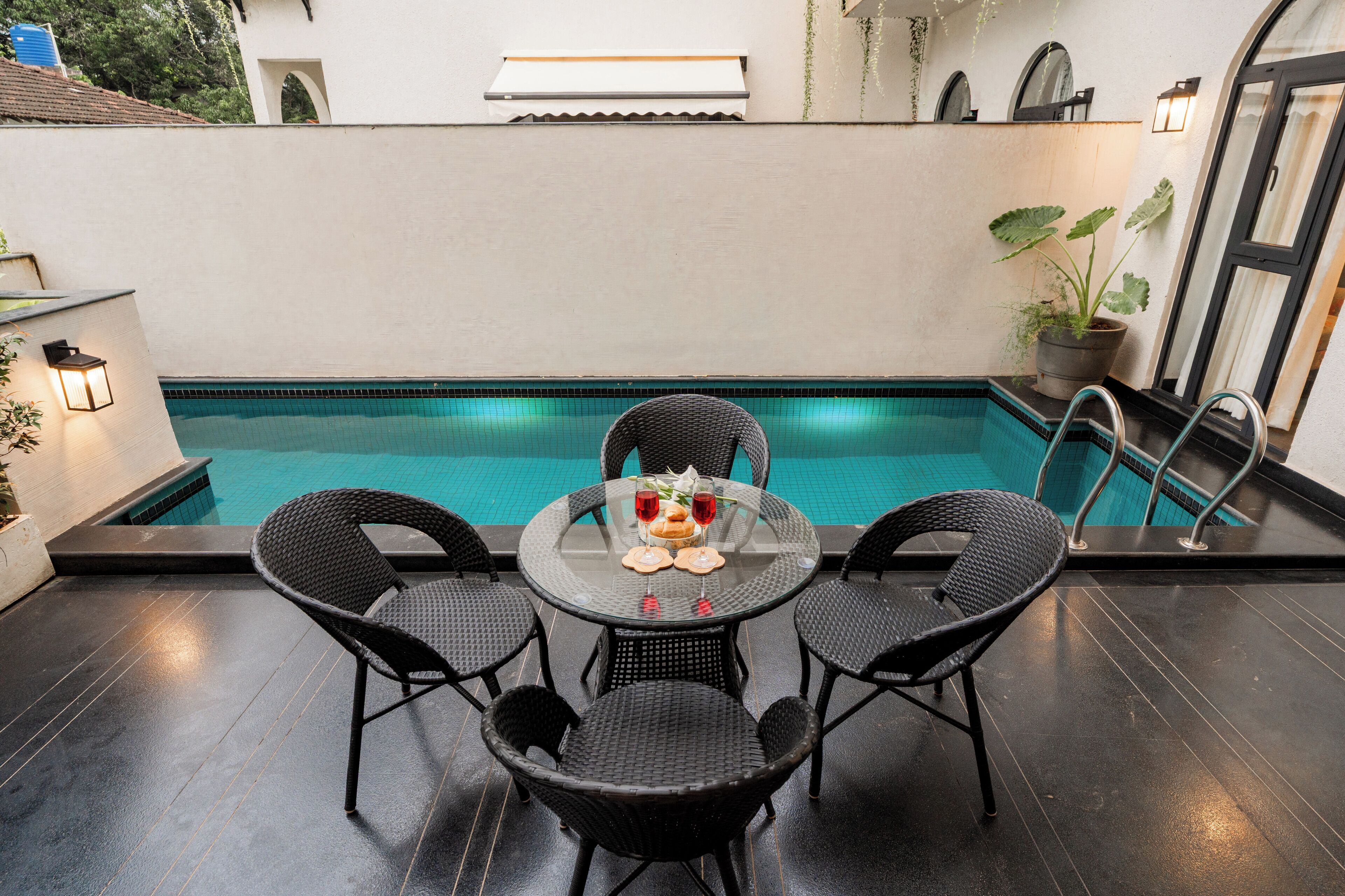 A poolside area with a round table and four chairs, a potted plant, and a view of a swimming pool.