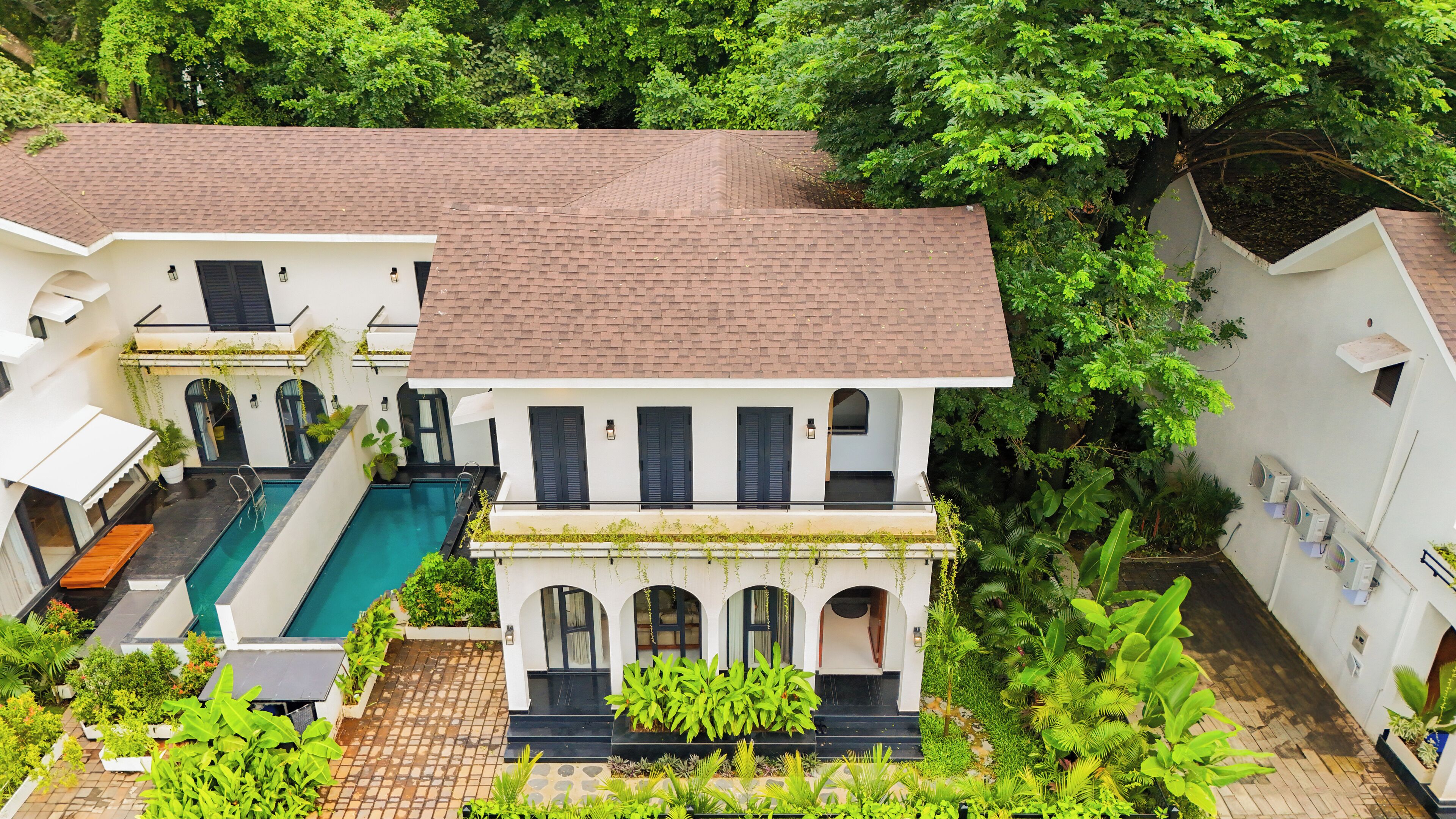 A two-story house with a swimming pool, surrounded by lush greenery.