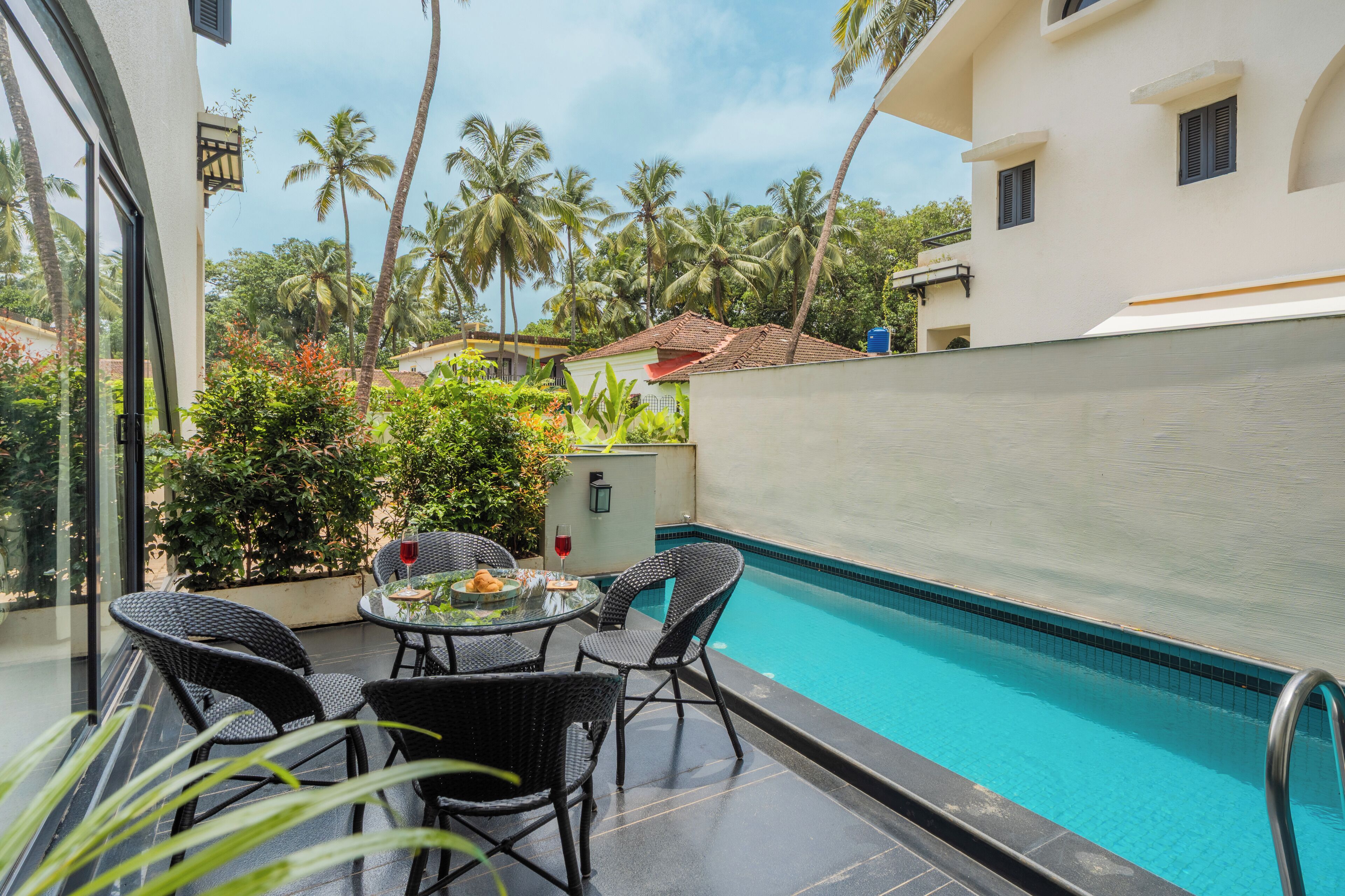 A poolside area with a table and chairs, surrounded by a pool and palm trees.