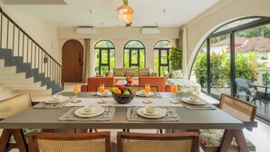 Un coin repas avec une table dressée pour quatre personnes, entourée de chaises en osier, et offrant une vue sur la verdure à travers de grandes fenêtres.