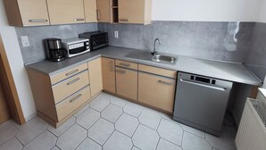 A compact kitchen with beige cabinets, a stainless steel dishwasher, and a microwave. - Cozy vacation apartment on the outskirts of Pirna in Saxon Switzerland (Pirna)