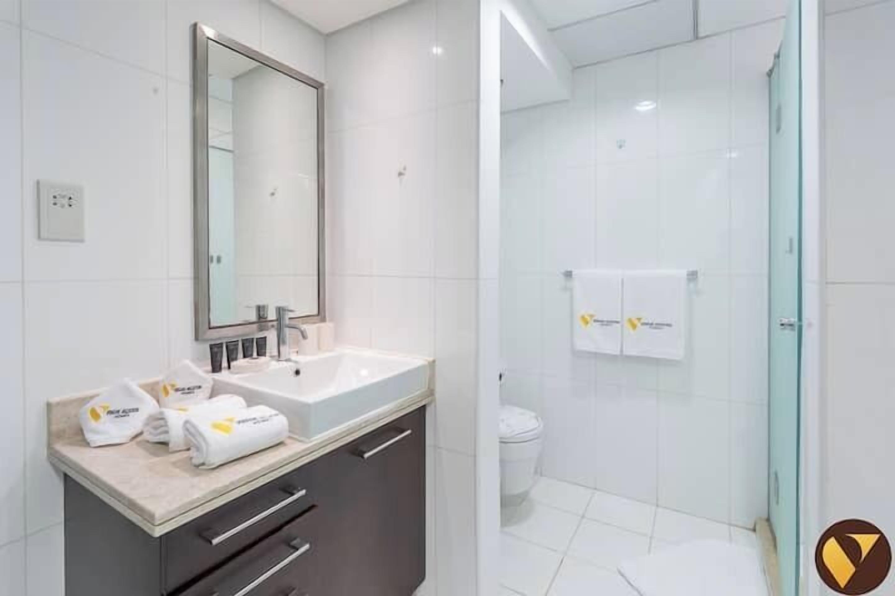 A modern bathroom with a large mirror, a sink, and a glass shower enclosure.