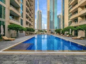 A swimming pool with lounge chairs, surrounded by high-rise buildings.