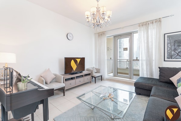 A modern living room with a piano, sofa, glass coffee table, and a TV.