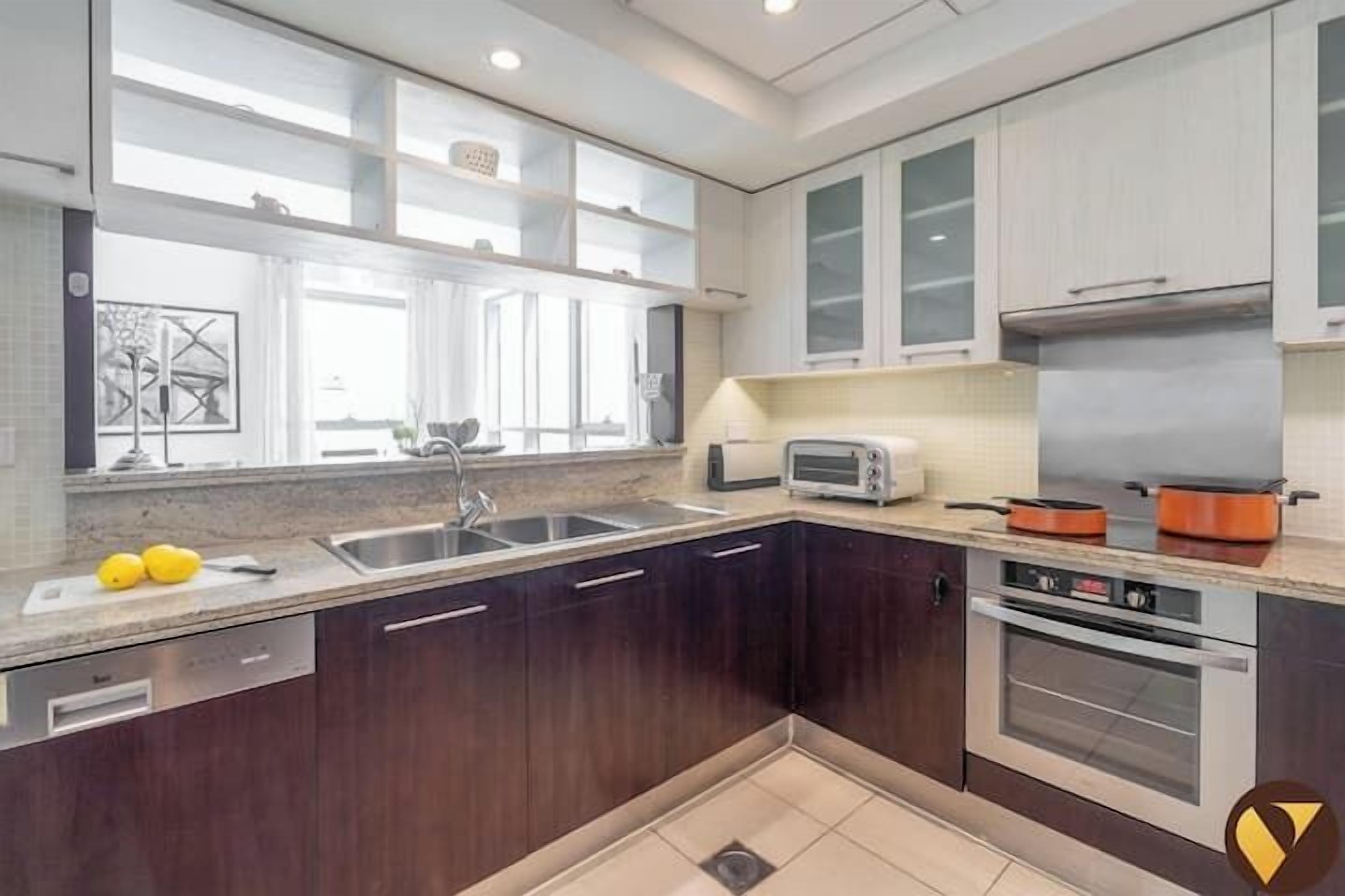 A modern kitchen with dark wooden cabinets, a stainless steel sink, a built-in oven, and a window providing natural light.