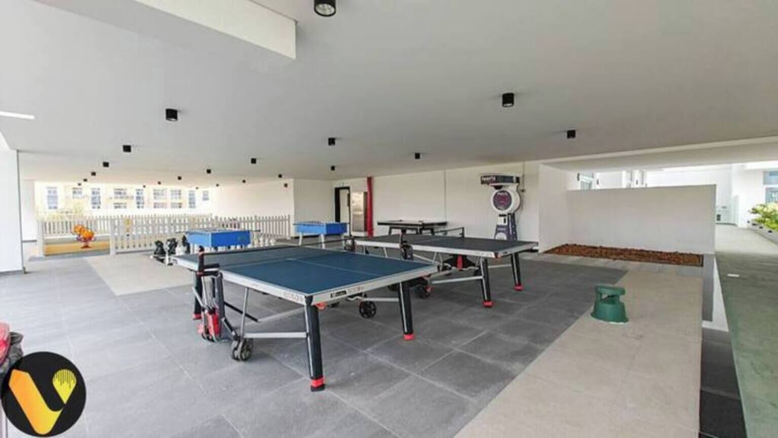 En inomhusanläggning för sportaktiviteter med flera bordtennisbord, ett vitt tak och ett klinkergolv.