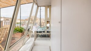 A modern balcony with a glass railing, a small table, and a potted plant.