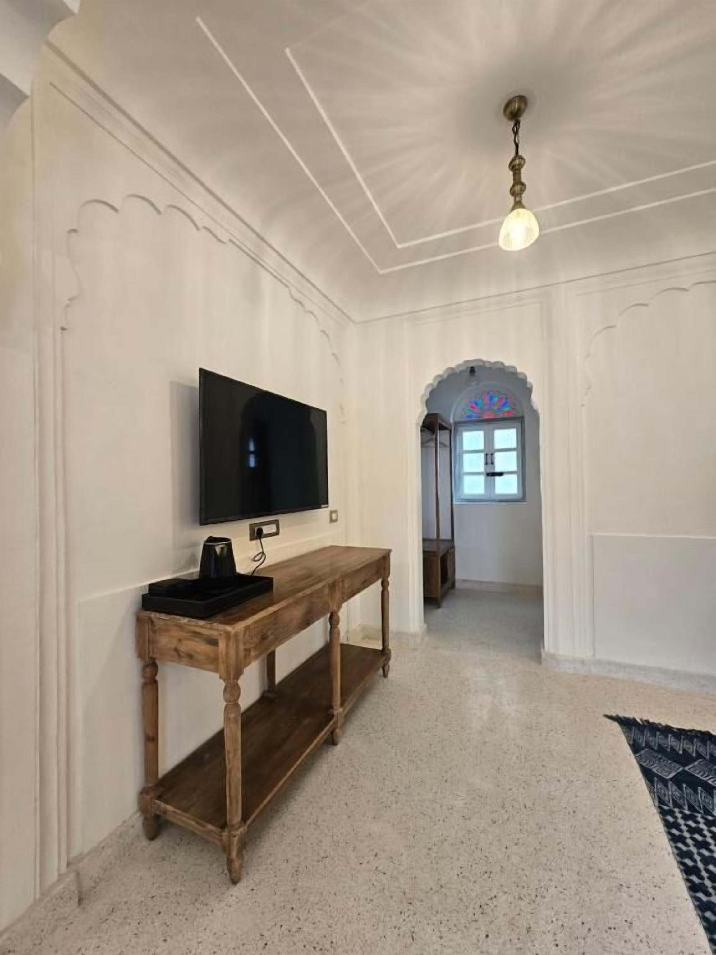 Quarto com televisão de tela plana na parede, mesa de console de madeira e tapete estampado no chão.