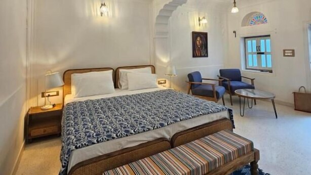 Une chambre spacieuse avec un grand lit, un banc, deux chaises, une table et une fenêtre donnant sur un beau paysage.