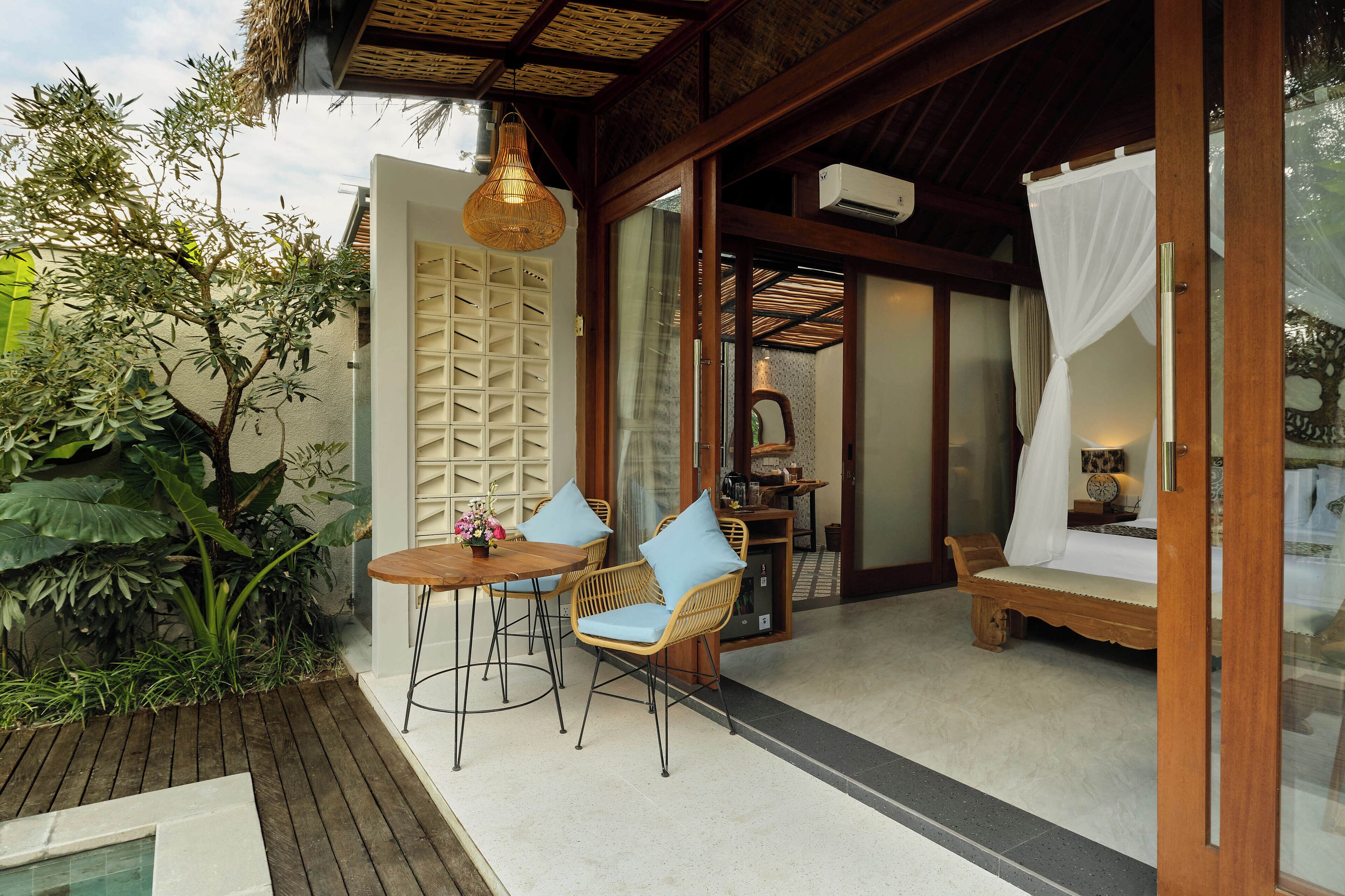 A cozy outdoor seating area with wicker chairs and a wooden table, a small pool, and a thatched roof structure.