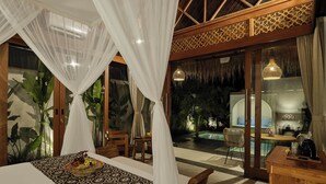 A bedroom with a bed, a bedside table, and a window overlooking a pool area. - Changi Jungle Ubud Villas (Ubud)