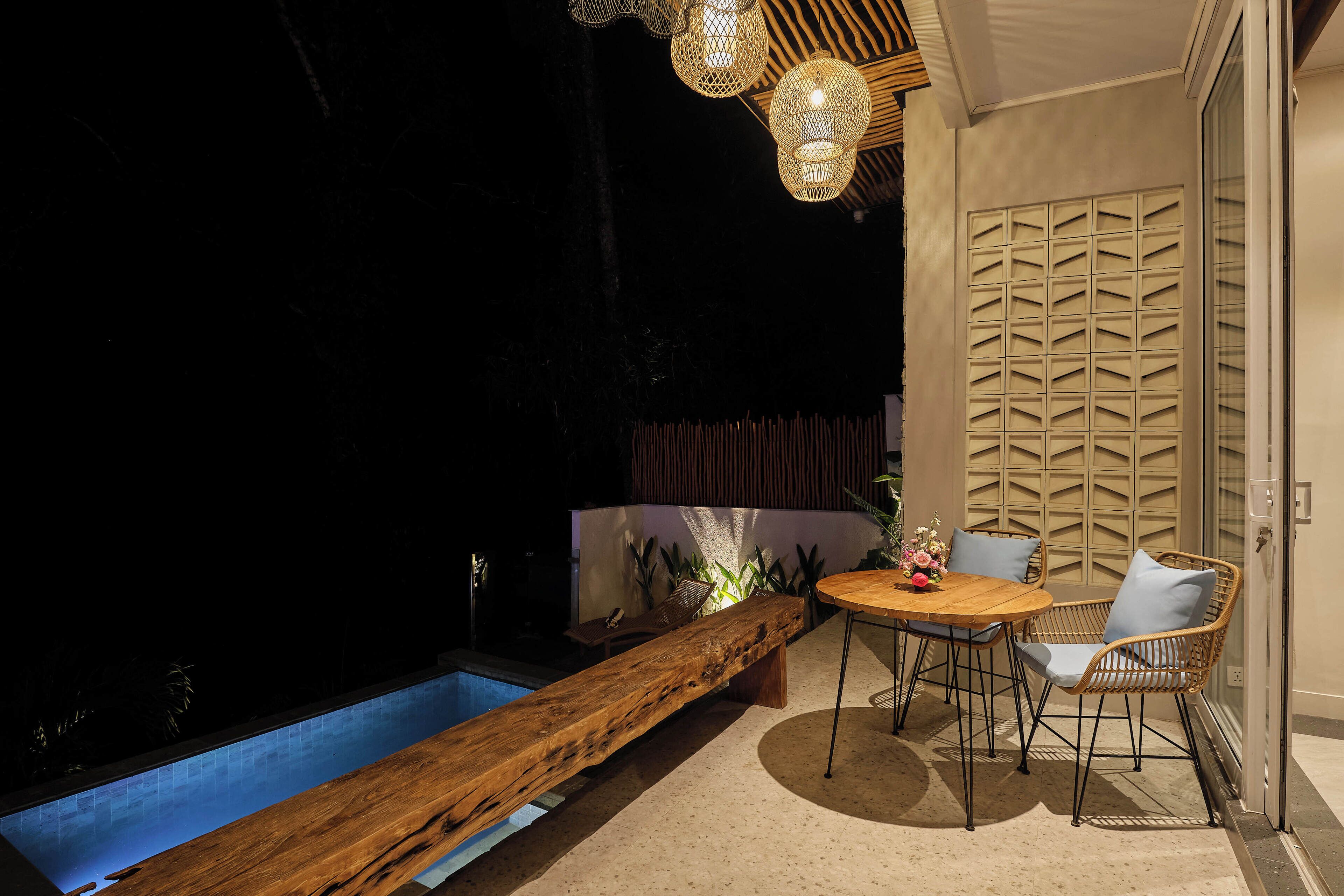 A poolside area with a wooden bench, a round table with chairs, and a decorative wall panel.
