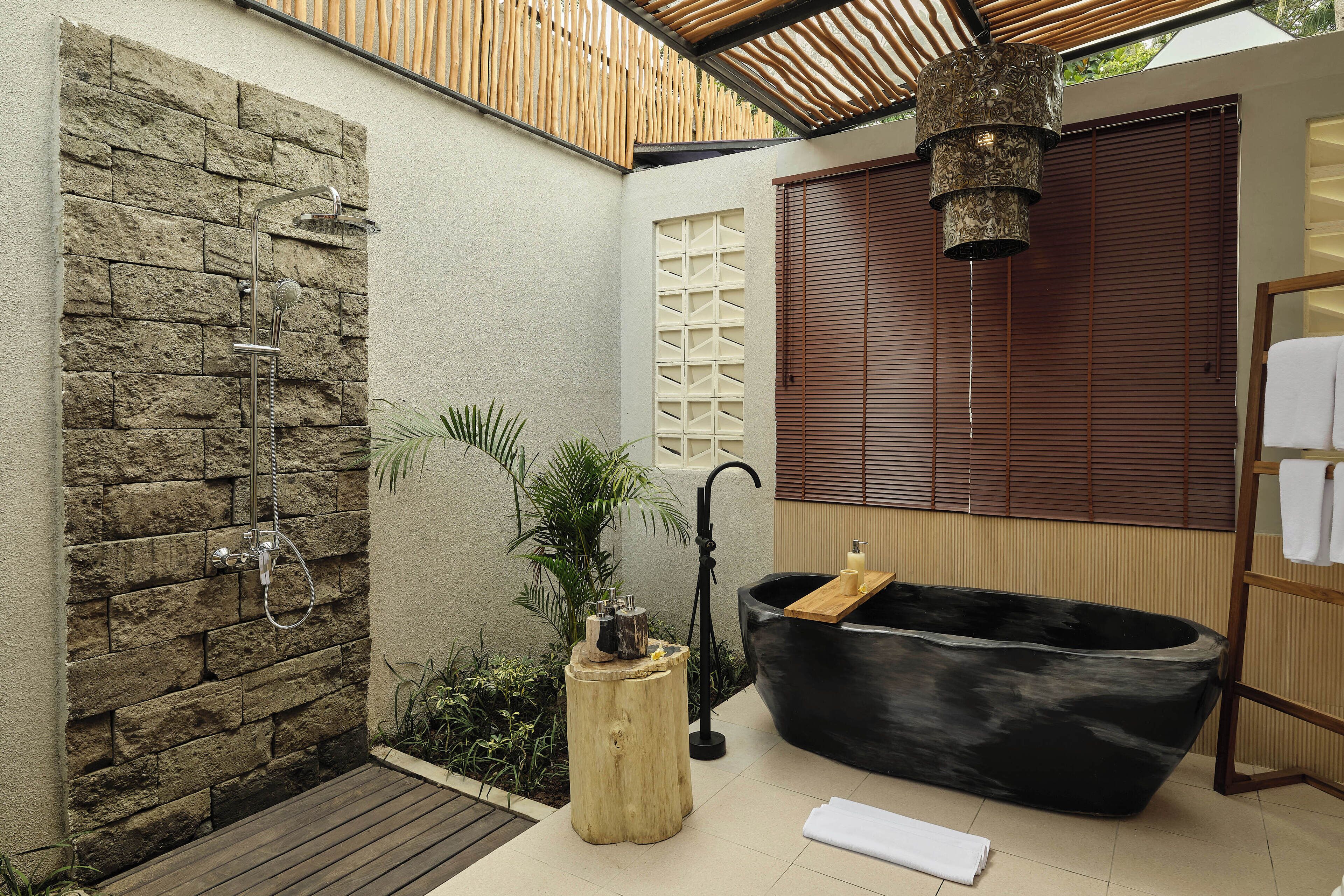 Un baño moderno con pared de piedra, una bañera independiente y un taburete de madera.