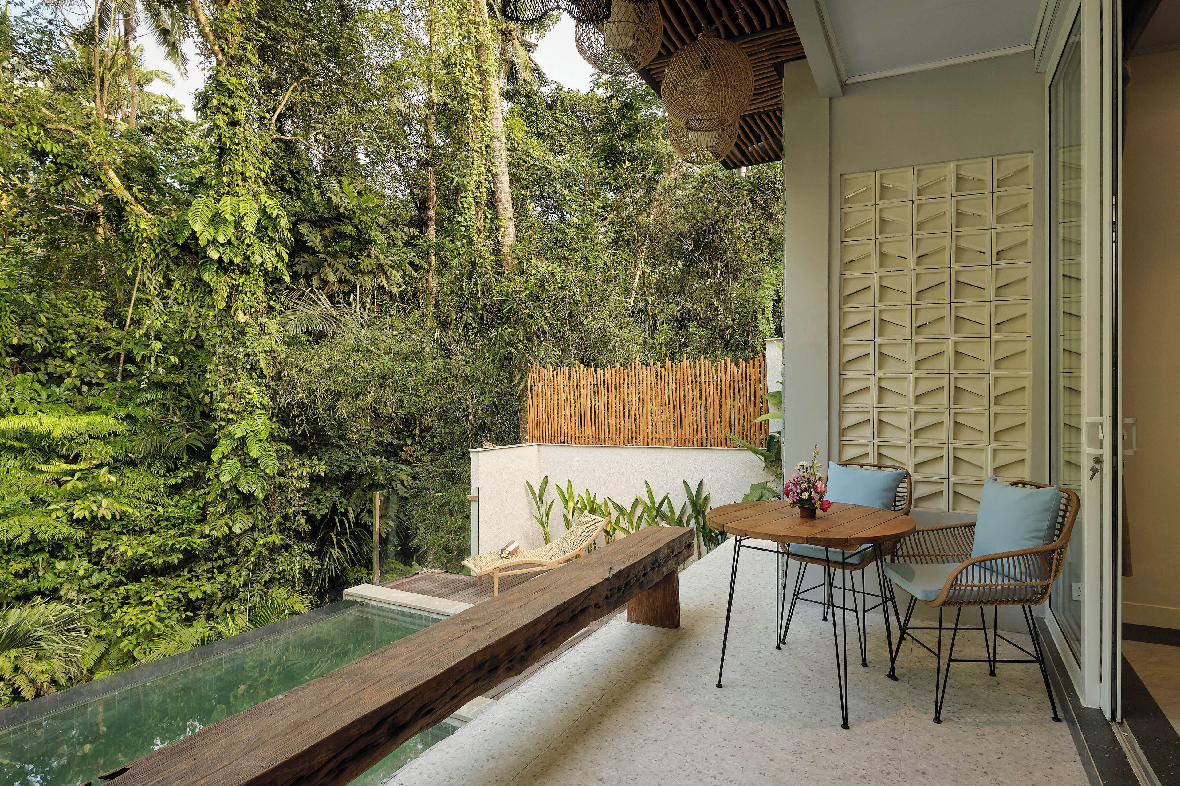 Een zwembadgedeelte met een houten terras, een tafel met stoelen en een uitzicht op weelderige begroeiing en een bamboombescherming.