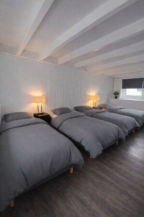 A room with four beds aligned in a row, each with a bedside table and lamp. - Boathouse Amsterdam with bikes (Amsterdam)