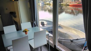 A modern room with a glass table and chairs, a view of a canal with boats, and a window overlooking the water. - Boathouse Amsterdam with bikes (Amsterdam)