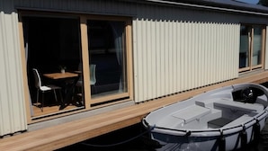 A boat docked at a house with a sliding glass door entrance, a small table with chairs, and a view of the water. - Boathouse Amsterdam with bikes (Amsterdam)