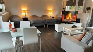 A modern living room with a sofa, two chairs, a coffee table, a TV, and a fireplace. - Boathouse Amsterdam with bikes (Amsterdam)