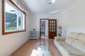 A living room with a sofa, a glass coffee table, a white shelving unit, and a wooden door leading to a kitchen. - Casa O Souto in Cangas (Vilanova)