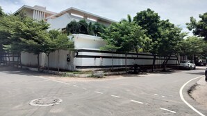 A parking lot with a large building in the background, surrounded by trees and a clear sky. - Truliv Villa Nova (Chennai)