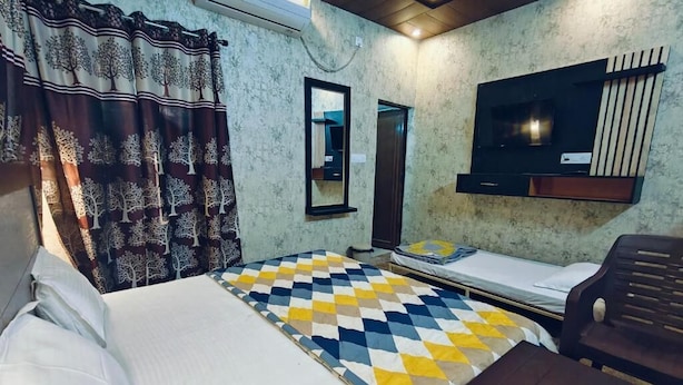 A room with a bed, a small table, a TV, and a mirror. - Shree Ji Inn Homestay (Rishikesh)