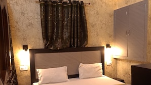 A bedroom with a bed, two bedside lamps, a wall-mounted air conditioner, and patterned curtains. - Shree Ji Inn Homestay (Rishikesh)