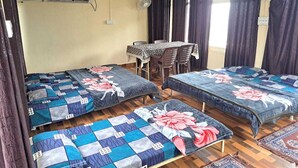 A room with two beds, a table, chairs, and two fans. - Shree Ji Inn Homestay (Rishikesh)