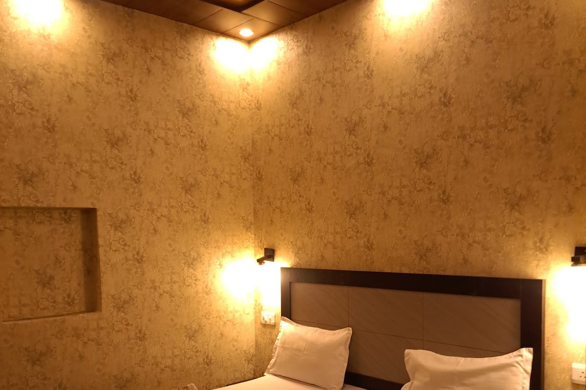 A neatly made bed with a patterned bedspread and two pillows, a headboard with a light fixture, and a textured wall with a recessed ceiling light.