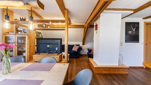 Un intérieur chaleureux avec un coin repas, des poutres en bois, un canapé et un téléviseur.