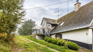 Une maison de campagne avec un toit en pente, une cheminée bien visible et un chemin menant à l’entrée.