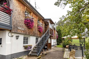 A wooden building with a staircase leading to a balcony, outdoor seating, and flower boxes. - Apartment 'On the Ground Floor' with Private Terrace, Shared Garden and Wi-Fi (Titisee-Neustadt)