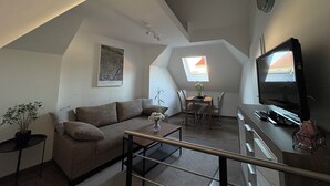 Ein Loft-Wohnzimmer mit hoher Decke, einem Essbereich mit Tisch und Stühlen, einer Couch, einem Couchtisch, einem Fernseher und einer Topfpflanze.