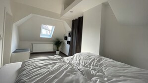 Ein Schlafzimmer mit schräg versiegelter Decke, einem Oberlicht, einer Heizung, einem Blumentopf und einem Bett.