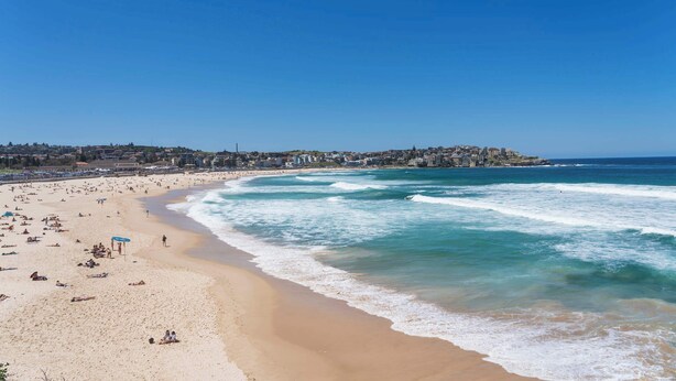 Una playa con una amplia orilla arenosa, olas rompiendo en la costa y un paisaje urbano distante.