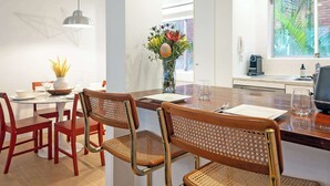 Un comedor moderno con una mesa redonda, sillas rojas, un florero con flores y una cocina al fondo.
