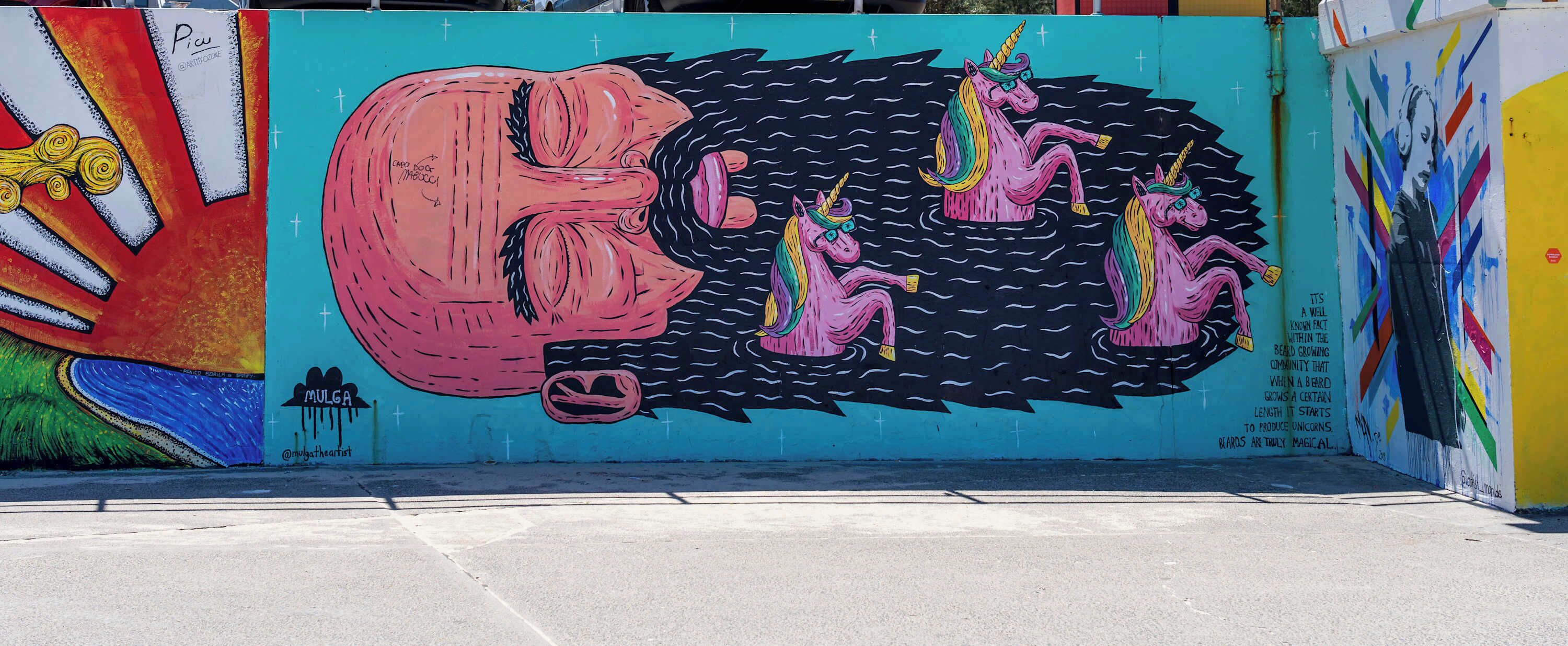 Un mural colorido con una figura rosa grande y unicornios en una pared.
