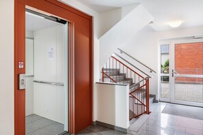 Vue intérieure du hall d’un hôtel, avec un escalier, une porte donnant sur un espace extérieur et un panneau indiquant qu’il est interdit de fumer.