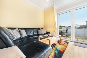 Un salon moderne avec un canapé en cuir noir, une table basse en verre et un tapis coloré.