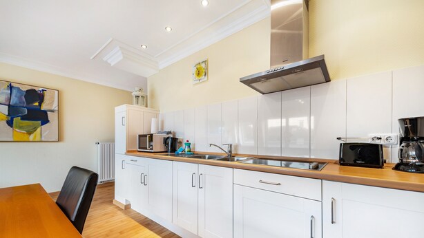 A modern kitchen with white cabinets, a wooden countertop, a coffee maker, and a microwave. - Apartment 'Duhnen' with Balcony and Wi-Fi (Cuxhaven)