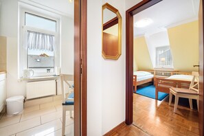 Ein Zimmer mit Bett, Stuhl, Tisch, einem Fenster mit Vorhängen, einem Heizkörper und einem Spiegel.