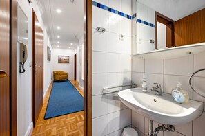 Un pasillo de hotel con alfombra azul, una puerta de madera, un teléfono y un cuadro en la pared.