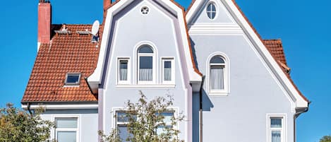 En tvåvåningsbyggnad med ett rött tegeltak, vita detaljer och många fönster.