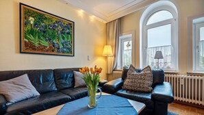 A living room with a black leather sofa, a coffee table with a vase of tulips, a painting on the wall, and a window with curtains.