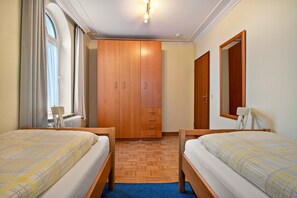 Una habitación de hotel con dos camas, un armario de madera, un espejo y una ventana con cortinas.