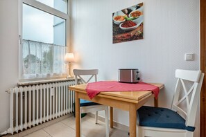 Una habitación pequeña con un radiador, una mesa con un tostador, una silla y una ventana con vistas.